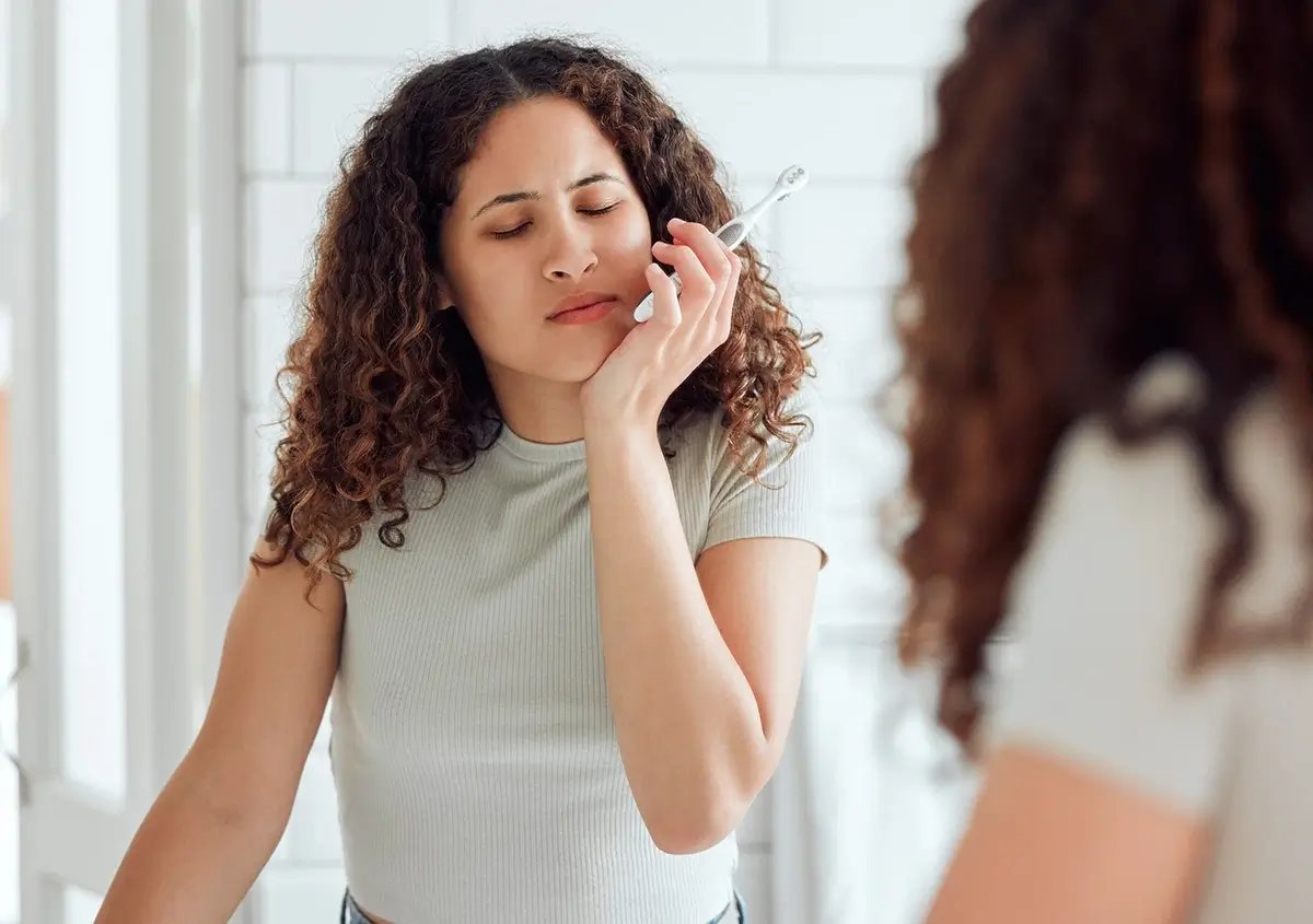 Young woman holding her jaw in pain while brushing her teeth, a common sign wisdom teeth may need to be removed